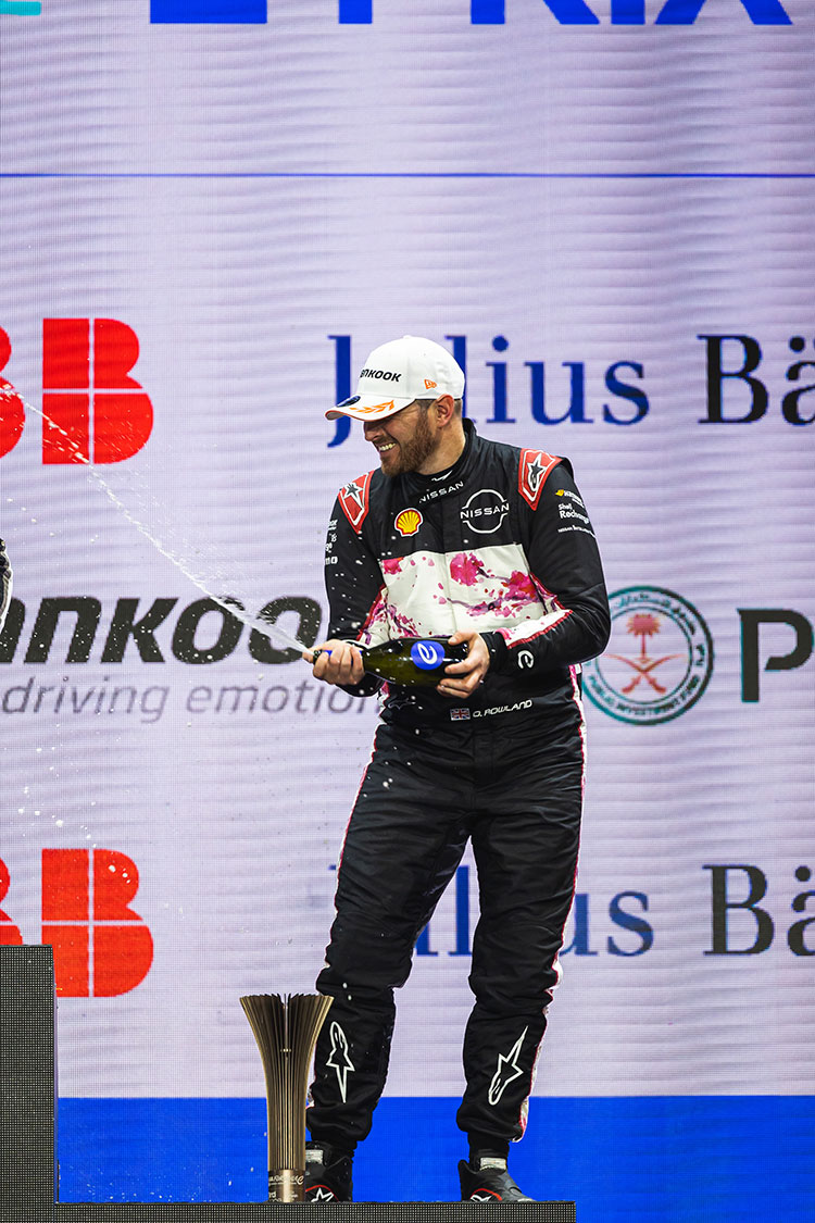 Un piloto del equipo de Nissan Fórmula E sonriendo en el podio, sosteniendo una botella abierta.