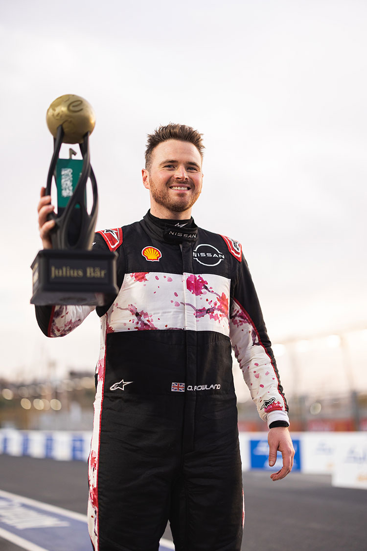 Un piloto del equipo de Nissan Fórmula E sonriendo en el podio, sosteniendo el trofeo.